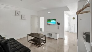 A modern living room with a black sofa, a wooden coffee table, a flat-screen TV, a white entertainment unit, and a door leading to another room. - NEW LISTING! Premium 2 bedroom/2bathroom Sleeps 7 (Miami)