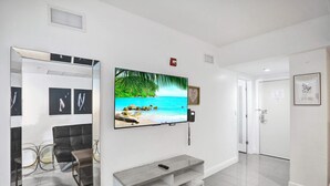 Een moderne woonkamer met een flatscreen televisie aan de wand, een grijze tv-kast eronder en een zwarte bank.