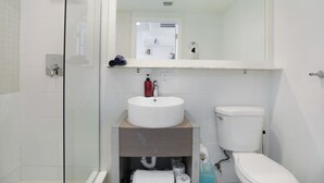 Un baño moderno con cabina de ducha de vidrio, un lavamanos blanco con un espejo encima y un inodoro.