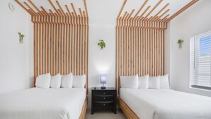 Habitación de hotel con dos camas, cabeceras de madera, una mesita de noche y una ventana con persianas.