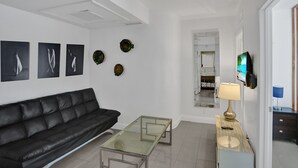 A modern living room with a black leather sofa, a glass coffee table, and a TV mounted on the wall.