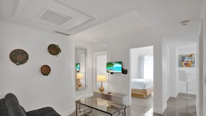 A modern hotel room with a glass coffee table, a sofa, a bed, and a TV on the wall.