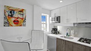 A modern kitchen with white cabinets, a stainless steel microwave, a coffee maker, and a gas stove. There is a glass table and a chair in the dining area.