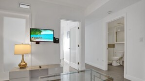 A modern bathroom with a toilet, a glass-enclosed vanity, and a mounted television displaying a beach scene.