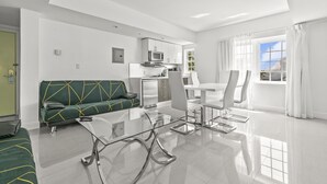 A modern living room with a glass coffee table, a green sofa, and a dining area with white chairs.