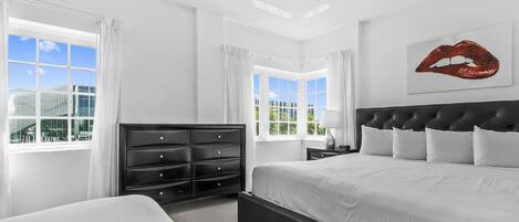Una habitación de hotel moderna con una cama grande, un aparador negro y vistas a un edificio a través de las ventanas.