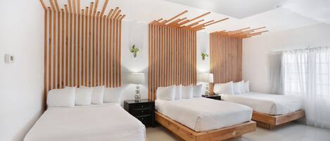 Una habitación de hotel moderna con tres camas, cabeceros de madera y un ventanal con cortinas de gasa.