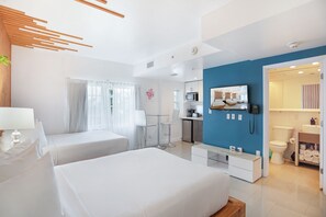 Una habitación de hotel con dos camas, kitchenette, baño y televisor.