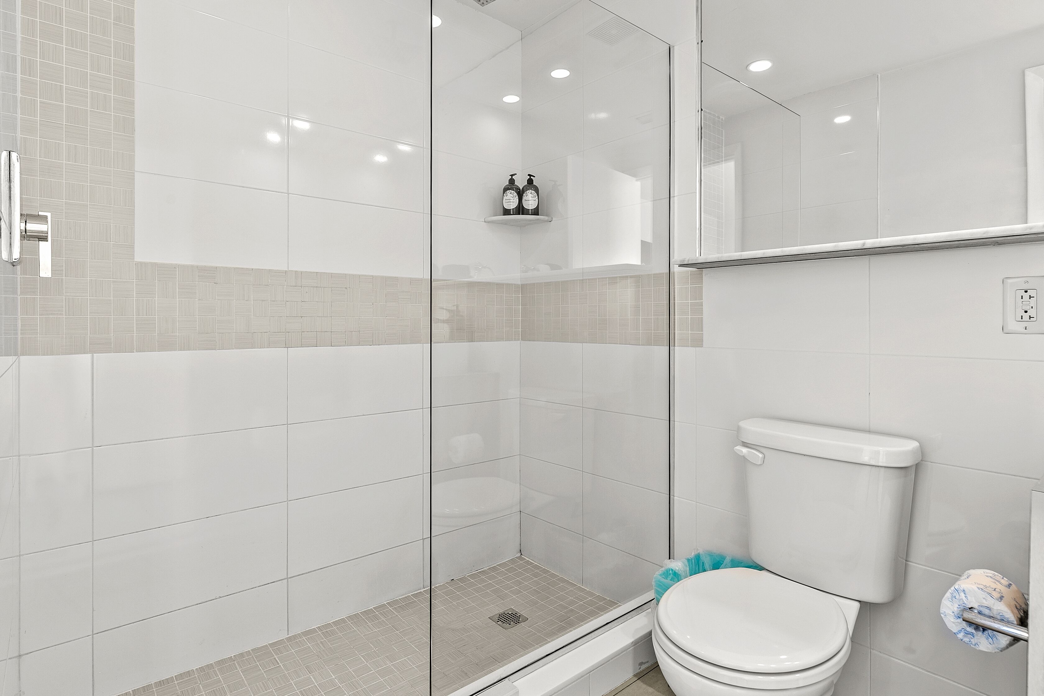 Een moderne badkamer met een douchecabine van glas, een toilet en een plank met toiletartikelen.