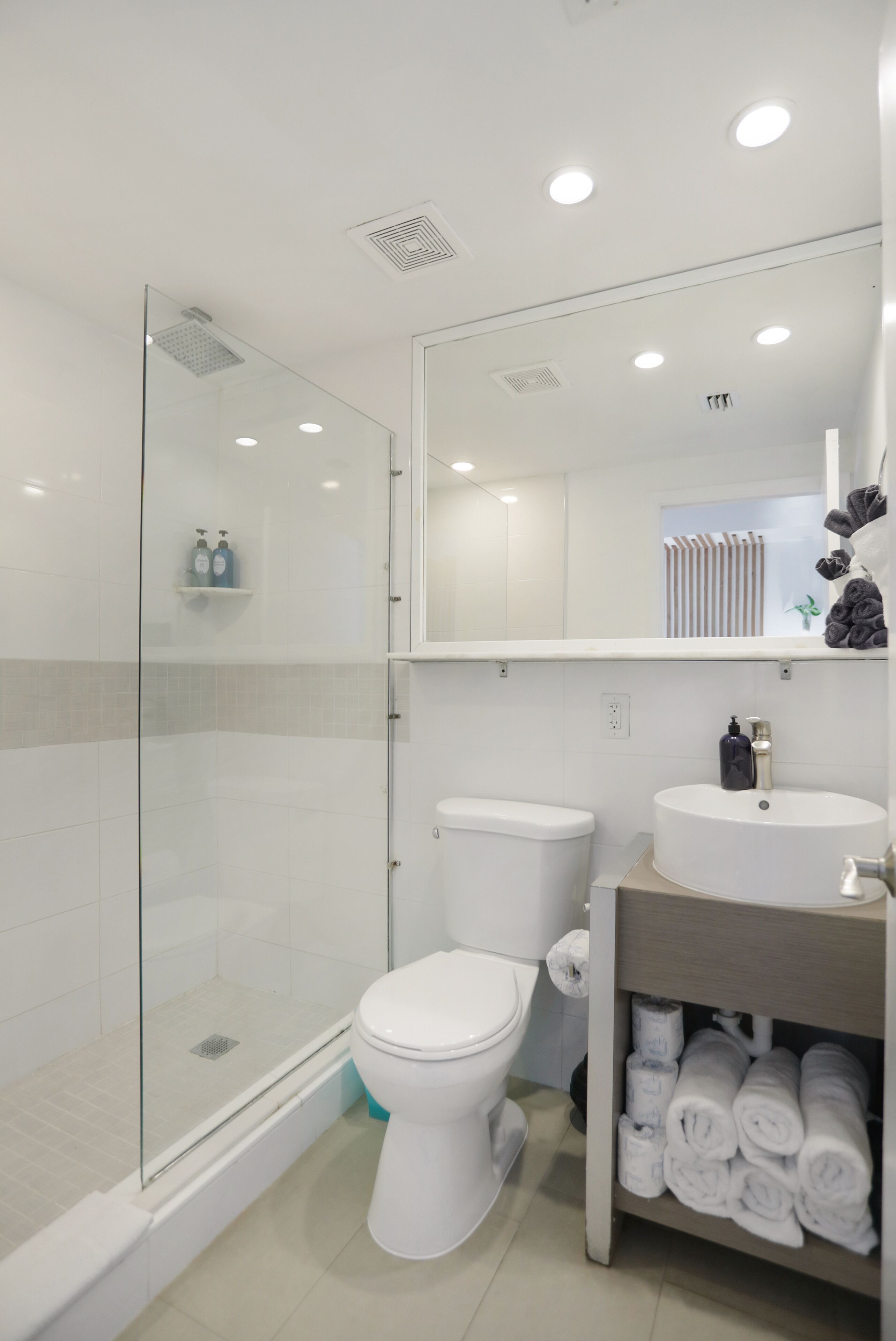 Un baño moderno con mampara de vidrio, inodoro, lavamanos y toallero con toallas dobladas con cuidado.