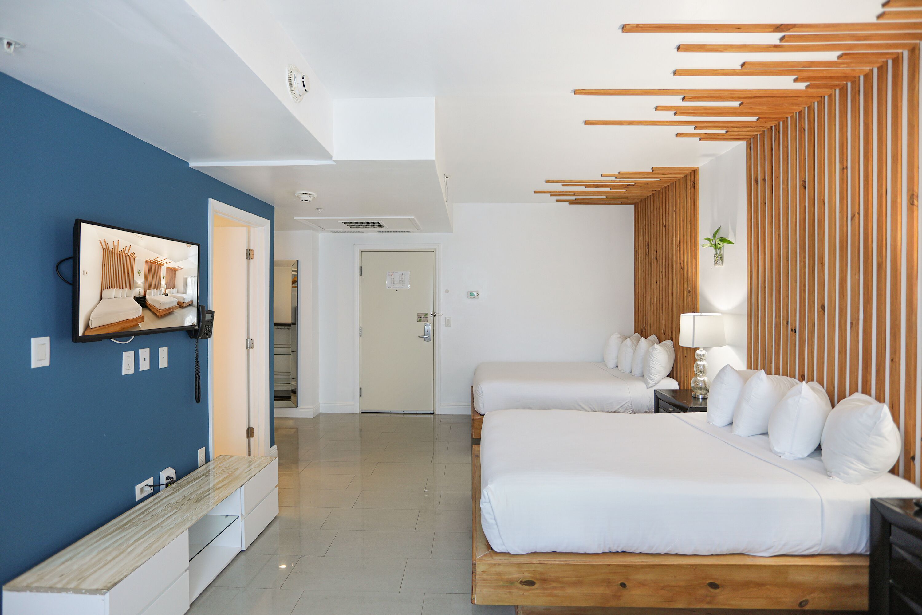 Une chambre d’hôtel moderne avec deux lits, une tête de lit en bois à lattes, un banc en marbre et un grand tableau au mur.