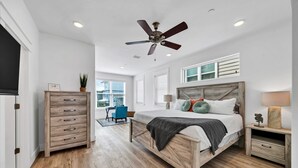 A bedroom with a wooden bed, a ceiling fan, a dresser, and a view of the outside. - Limited time-10% off of Summer25! New 5bd/5b-5 min walk to bch/rooftop/ 5 park  (Santa Rosa Beach)