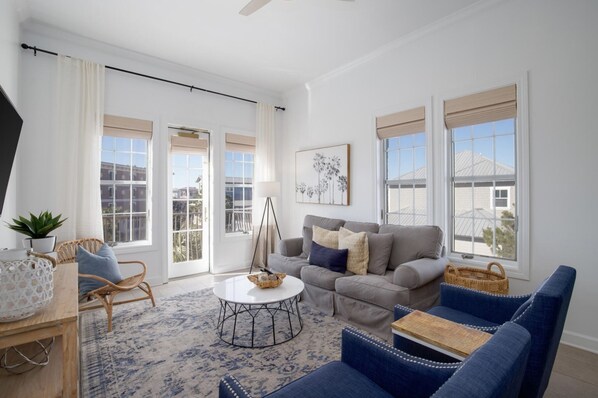 Un salón amplio con un sofá gris, sillones azules, una mesa de centro y un ventanal con vistas a edificios.