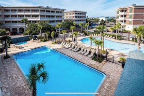 A hotel with multiple swimming pools, palm trees, and a clear blue sky.