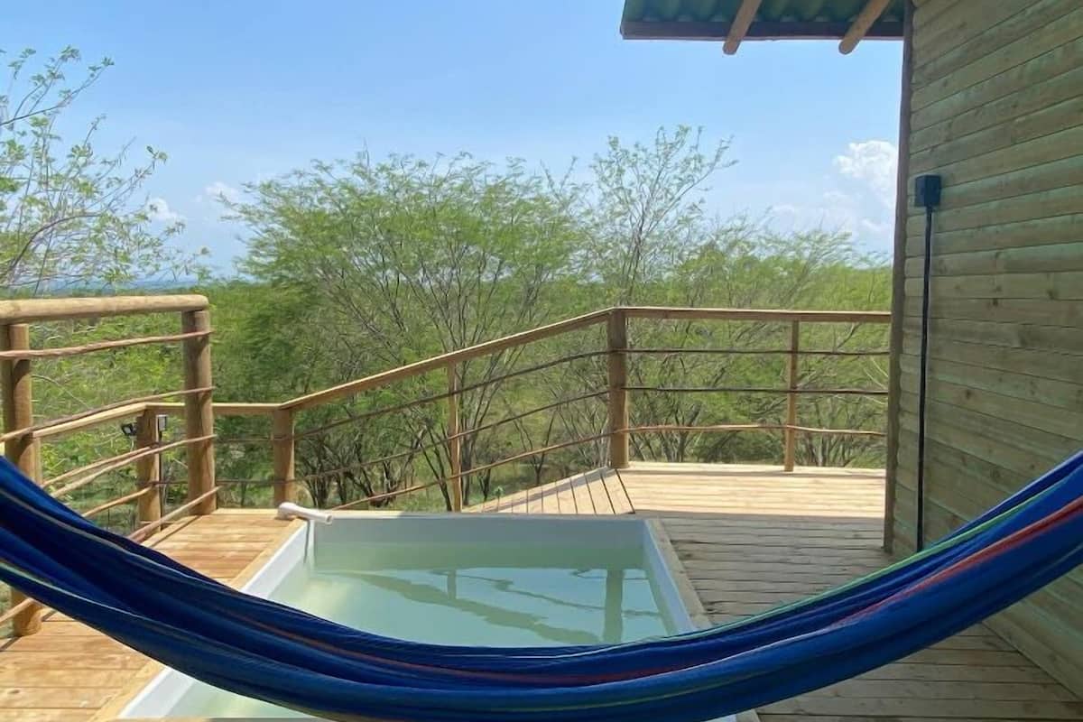 A wooden deck with a glass-enclosed hot tub and a hammock.