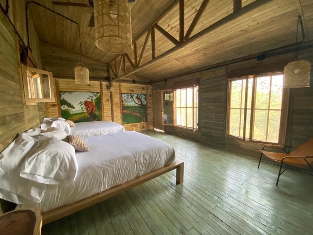 A wooden cabin bedroom with a large bed, a chair, and a painting on the wall.