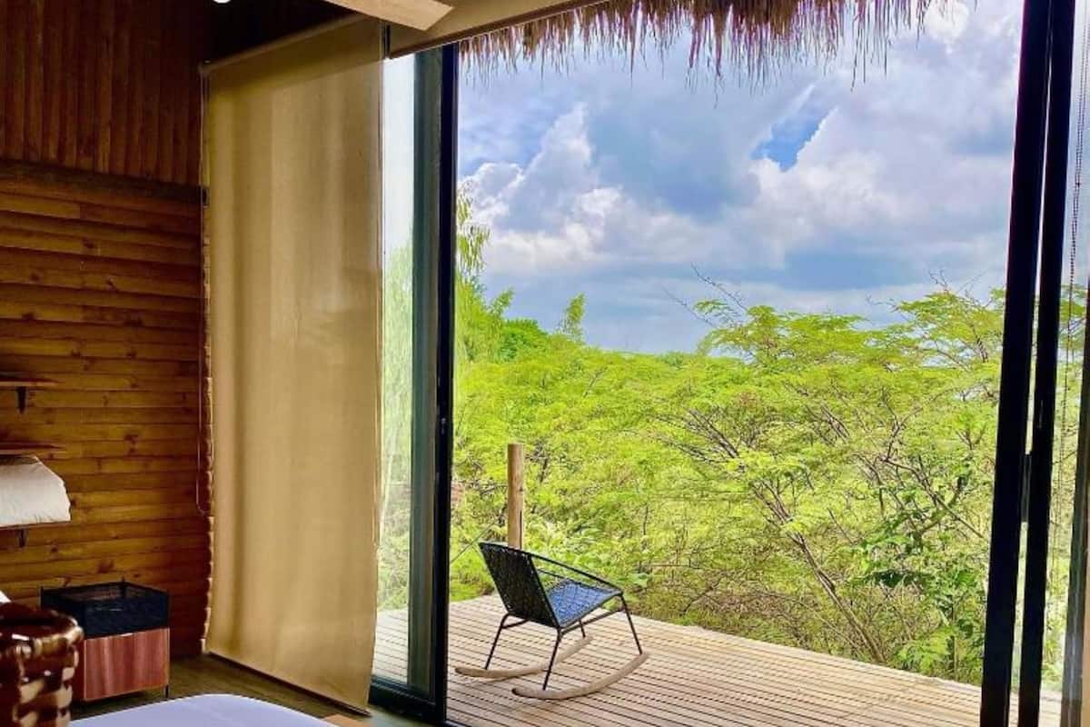 A room with a bed, a chair, and a large window with a view of trees.