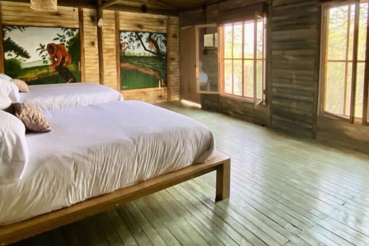 A spacious bedroom with a large bed, wooden beams, and a mural on the wall.