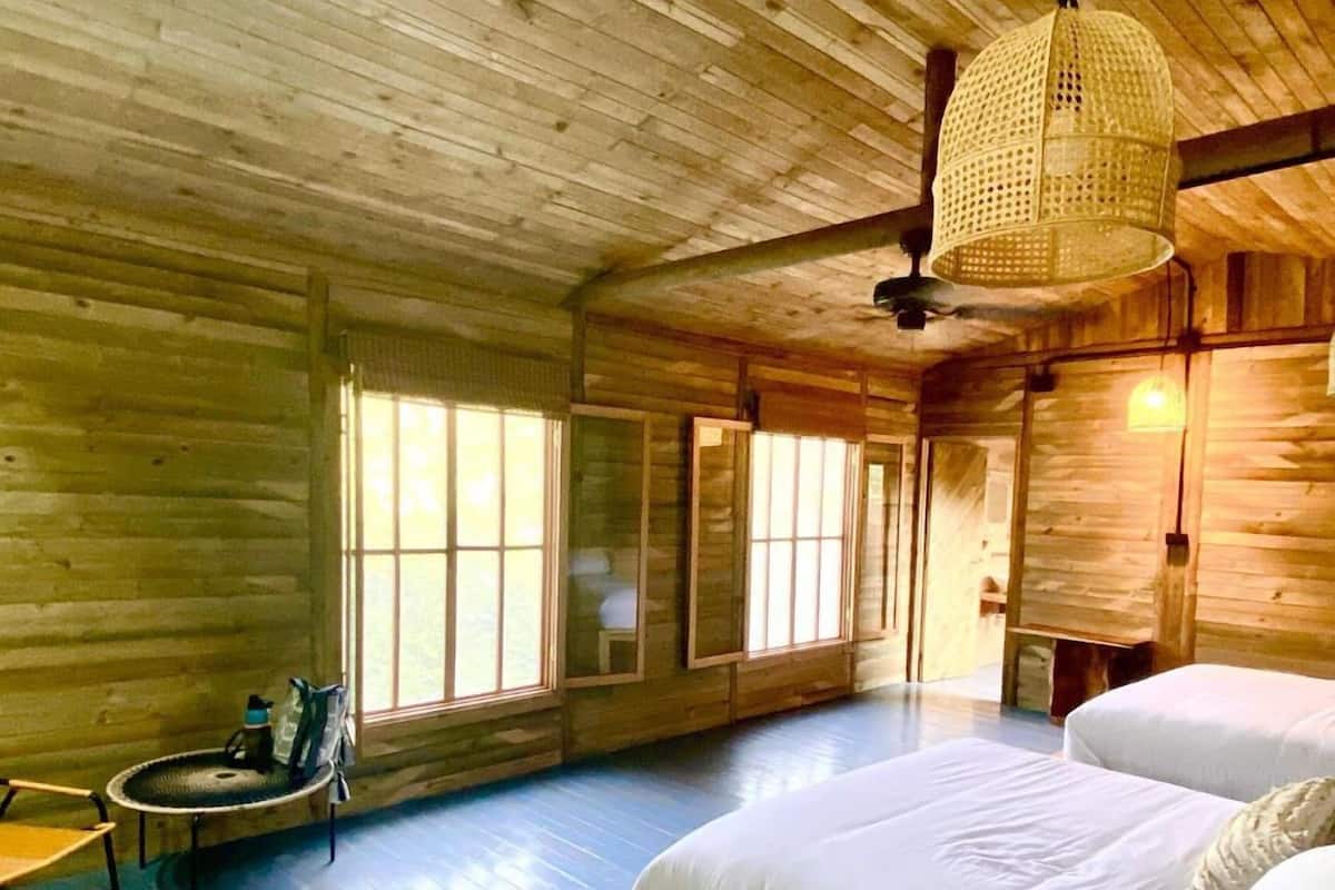 A wooden cabin room with a large bed, a small table, and a hanging light fixture.