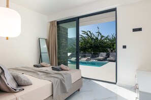 A modern bedroom with a large bed, a glass door leading to a pool area, and a view of the outdoors. - Luxurious villa with a large pool, 750m from the beach. (Asprouliani)
