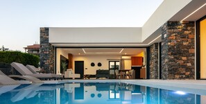 A modern house with a swimming pool, stone walls, and a dining area. - Luxurious villa with a large pool, 750m from the beach. (Asprouliani)