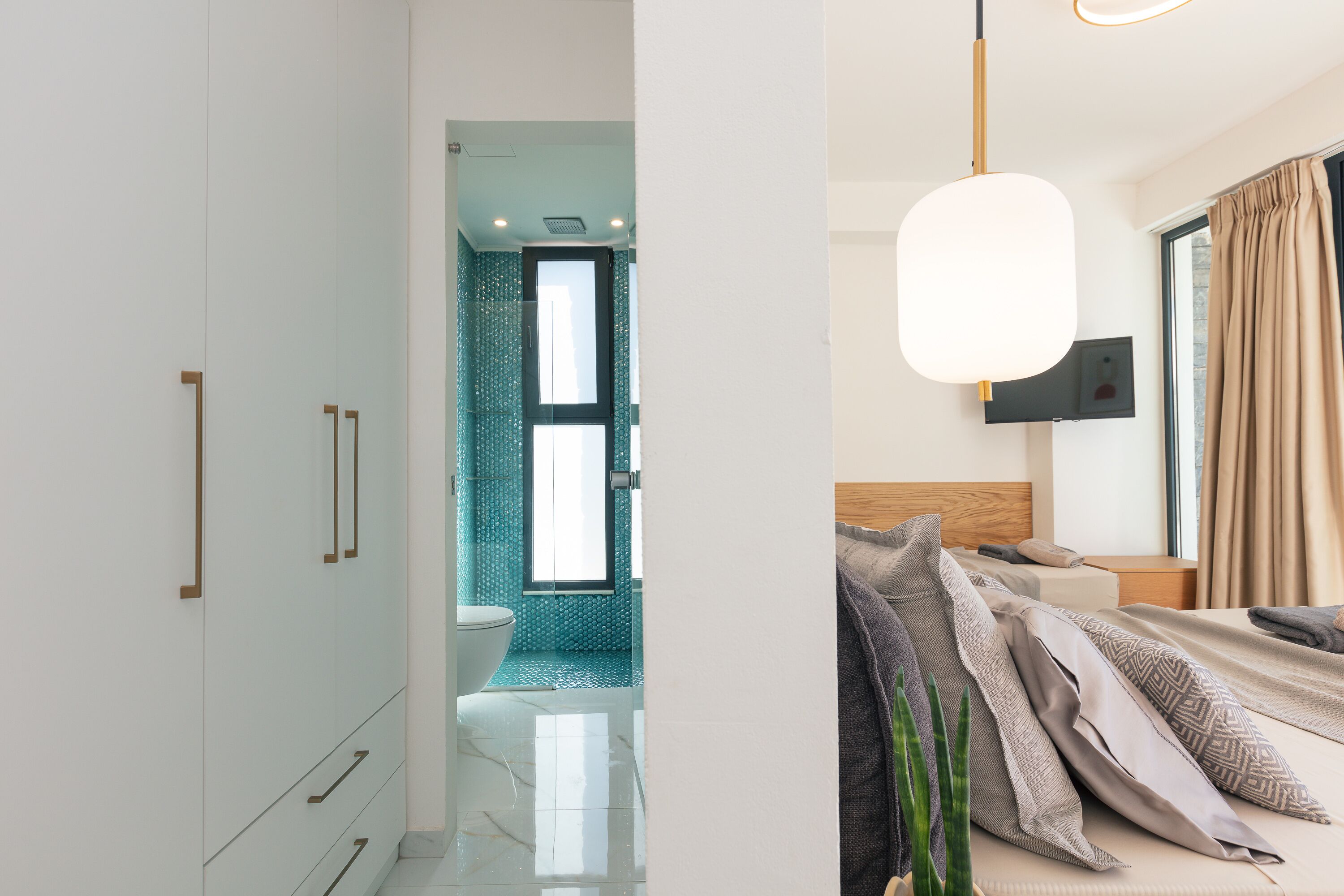 Ein modernes Schlafzimmer mit Bett, Nachttisch und Blick auf ein Badezimmer mit Toilette und Dusche.