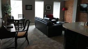 Uma sala de estar com sofá, mesa de jantar e cadeiras, televisão e parede de tijolos.