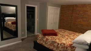 Quarto com cama, espelho, armário e parede de tijolos.