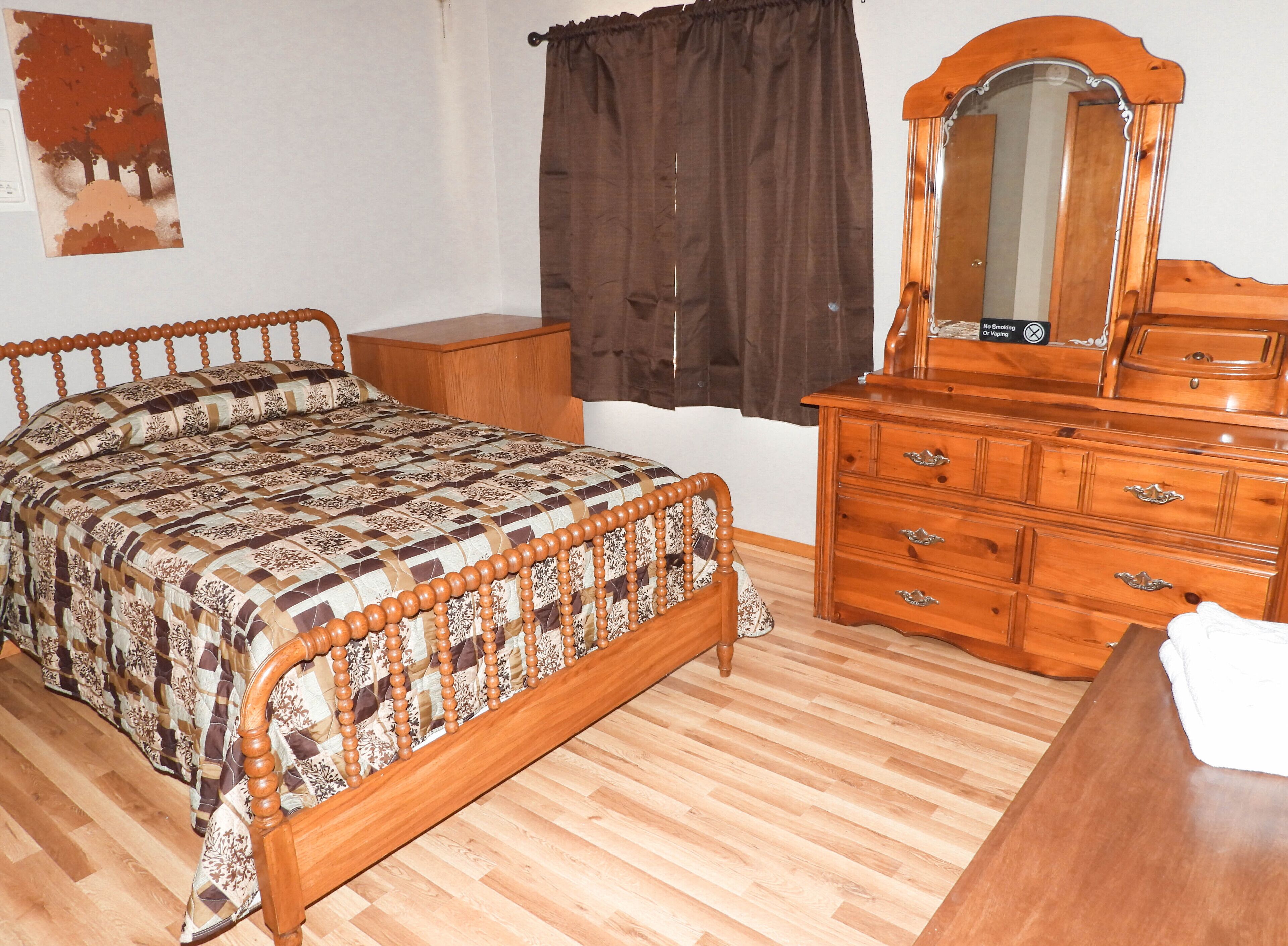 Een slaapkamer met een houten bed, een dressoir en een spiegel.