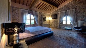 A bedroom with a large bed, stone walls, a stone fireplace, a TV, and a chair. - Room in B&B - Room Overlooking the Vineyards and Florence (Carmignano)