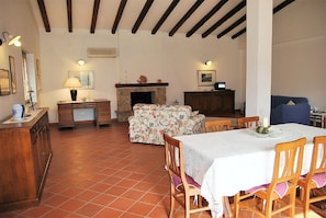 A dining area with a table set for four, wooden chairs, a floral sofa, a fireplace, and a wooden cabinet.