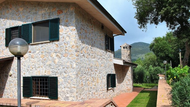 A stone building with multiple windows and shutters, a paved pathway, and a view of a hill. - Villa Il Casolare Country House With Pool on Sperlonga's Hill (Itri)