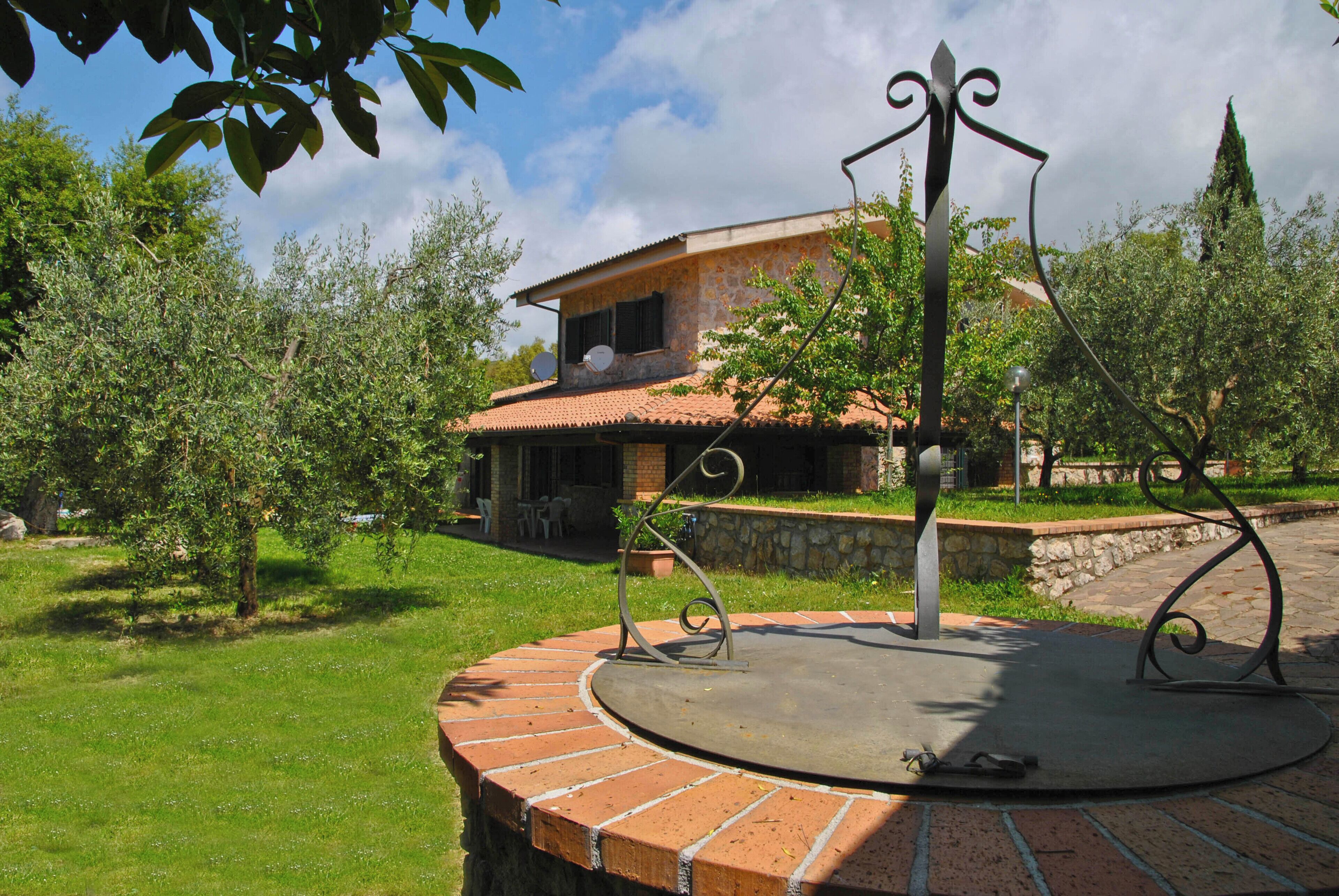 A house with a stone facade, a tiled roof, and a circular patio with a metal sculpture.