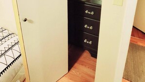 Un pasillo estrecho con una puerta a la izquierda, suelo de madera y un armario negro con cajones.