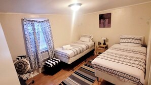Un dormitorio con dos camas, una ventana con cortinas estampadas, una mesita de noche con lámpara y un cuadro en la pared.