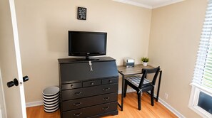 A room with a television on a dresser, a desk with a chair, a small potted plant, and a window with blinds. - Room-black-white Rm By Yale U (New Haven)