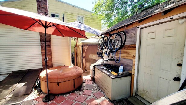 Ein Garten mit einer Terrassenfläche, einem Whirlpool, einem überdachten Sitzbereich und Fahrrädern, die an der Wand befestigt sind.