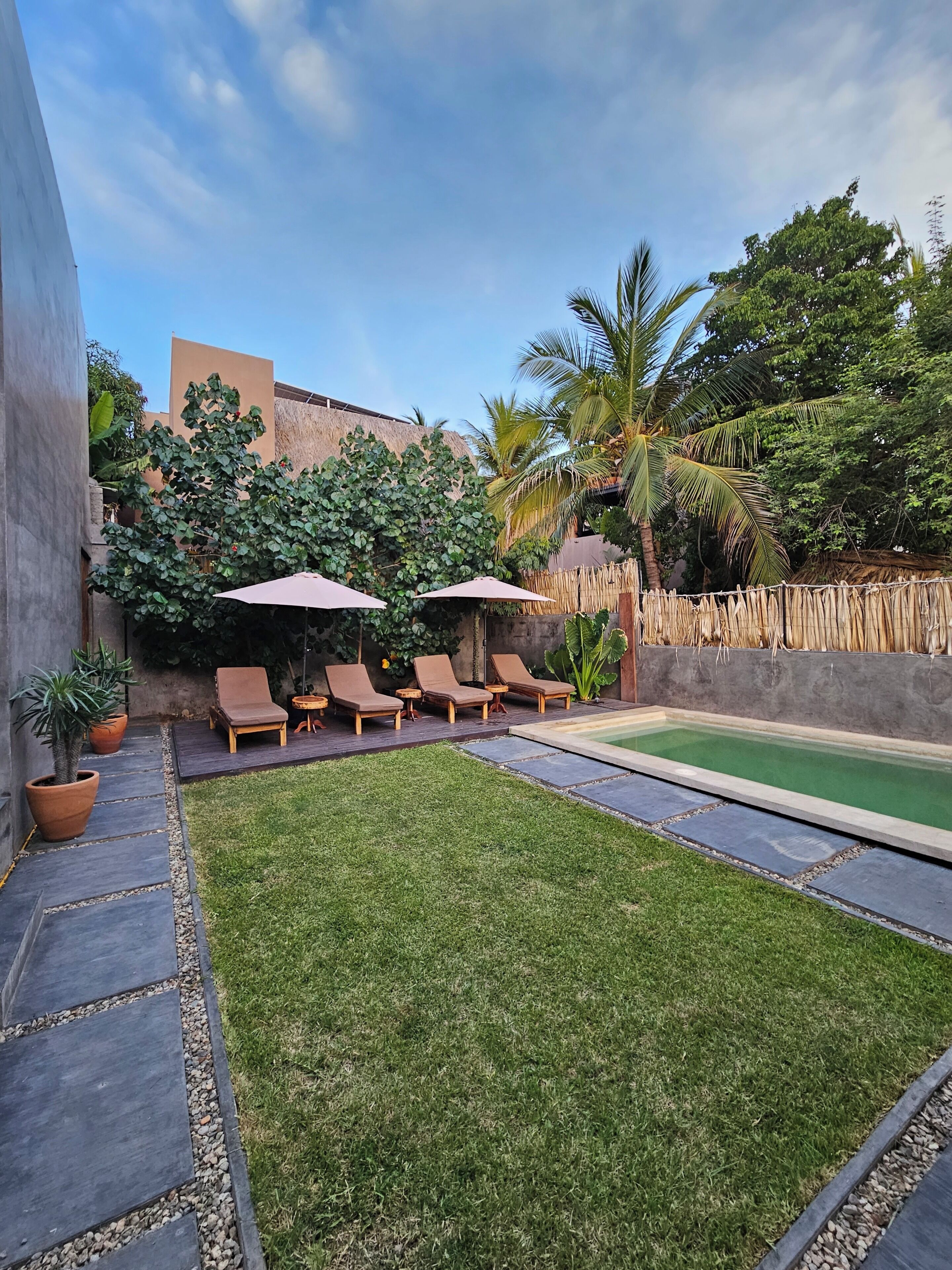 A backyard with a swimming pool, lounge chairs, and a small garden area.