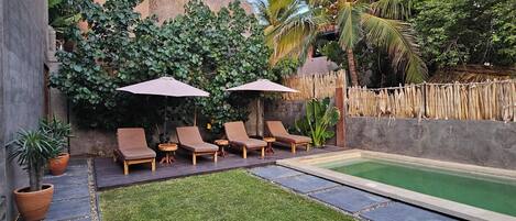 A backyard with a swimming pool, lounge chairs, and a small garden area.
