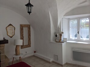 Ein Zimmer mit weißer Wand, einem spiegelnden Holzrahmen, einer hängenden Laterne, einem Fenster mit weißem Rollo und einem Heizkörper.