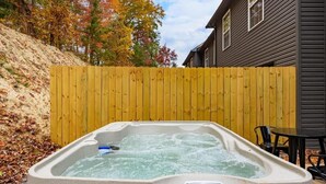 Ett bubbelbad i en trädgård med ett staket av trä och ett hus i bakgrunden.