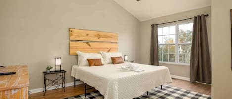 A bedroom with a large bed, a ceiling fan, a window with curtains, and a checkered rug.