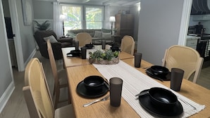 A dining area with a wooden table set for four, surrounded by chairs. A chandelier hangs above, and a kitchen is visible in the background. - 4 Bedroom Retreat Sleeps 11 with Dock on Lake Weir near The Villages & Orlando (Summerfield)