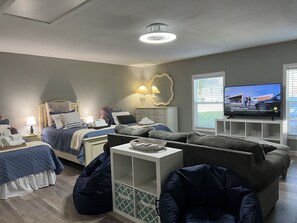 Un dormitorio moderno con cama, mesitas de noche, televisor y zona de estar con sofá y sillón de peluche.