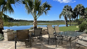 An outdoor patio with a table and chairs, a stone wall, and a view of a lake and trees. - 4 Bedroom Retreat Sleeps 11 with Dock on Lake Weir near The Villages & Orlando (Summerfield)