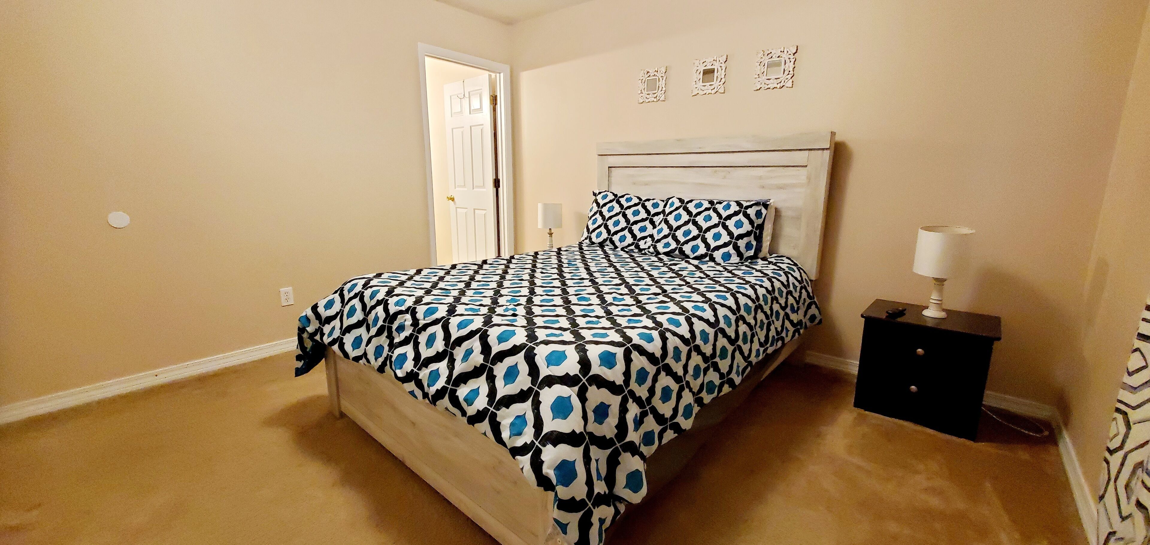 A bedroom with a bed, a nightstand, a door, and wall decorations.