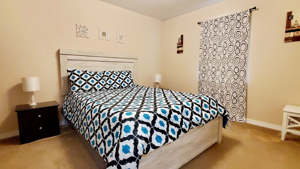 Un dormitorio con cama, mesita de noche y un pequeño banco blanco.