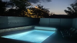 Una piscina rectangular con fondo de cristal, rodeada por un muro de piedra y una cerca de metal.