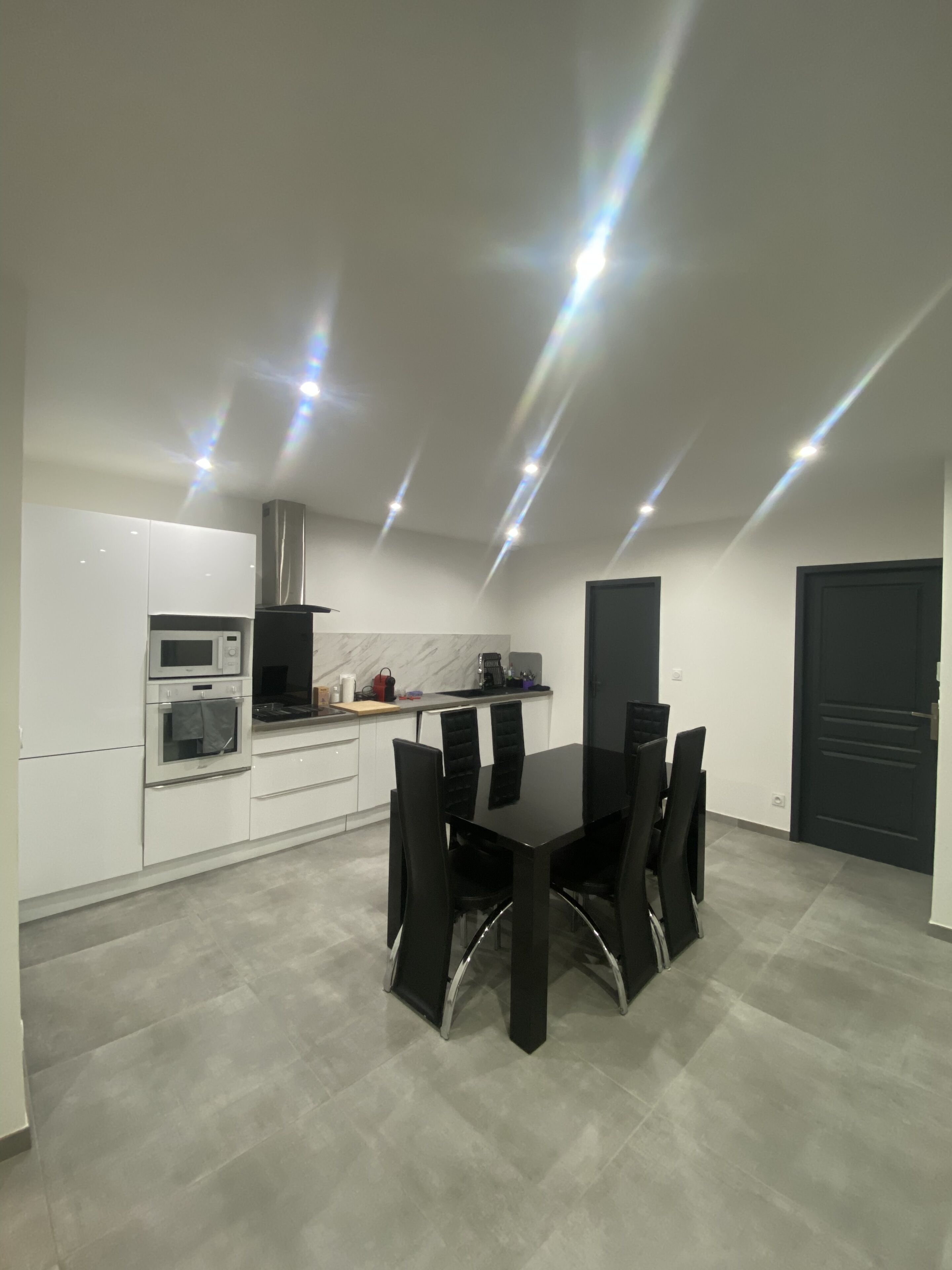 A modern kitchen with white cabinets, a black dining table with chairs, and a black door.