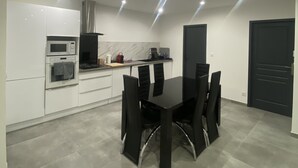 Una cocina moderna con armarios blancos, una mesa de comedor negra y sillas, y una puerta negra.
